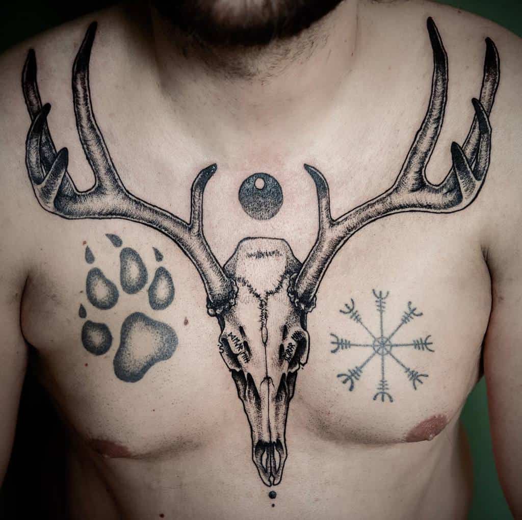 A man's chest adorned with tattoos featuring a deer skull, paw print, and intricate geometric patterns
