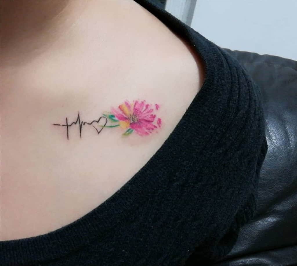 A delicate tattoo on the chest featuring a heartbeat line transitioning into a heart, with a vibrant pink flower next to it, symbolizing faith, hope, love, and beauty