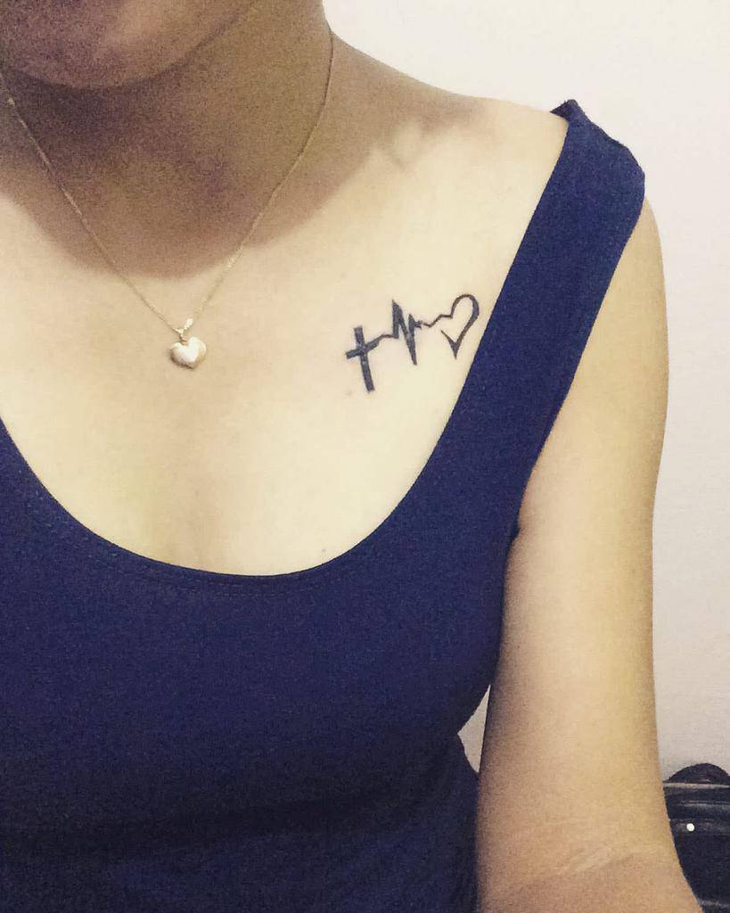 Woman with a chest tattoo symbolizing faith, hope, and love—a cross, heartbeat line, and heart