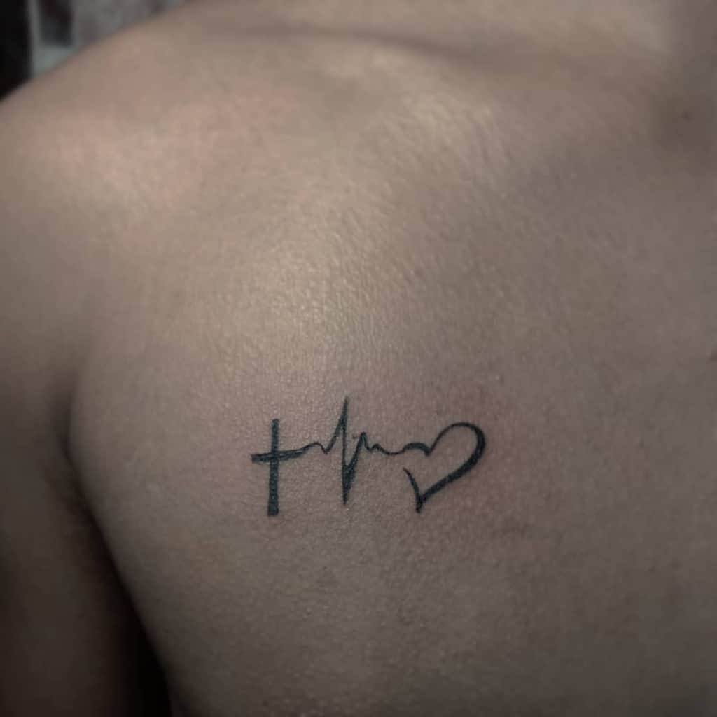 A minimalist tattoo graces the person's shoulder, featuring a cross for faith, a heartbeat line symbolizing hope, and a heart for love—all elegantly etched in black ink