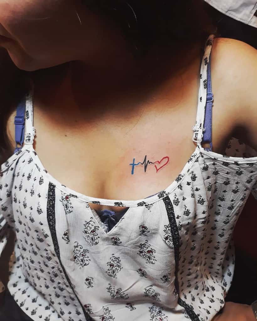 A woman with a tattoo of a cross, heartbeat line, and heart graces her upper chest, symbolizing faith, hope and love