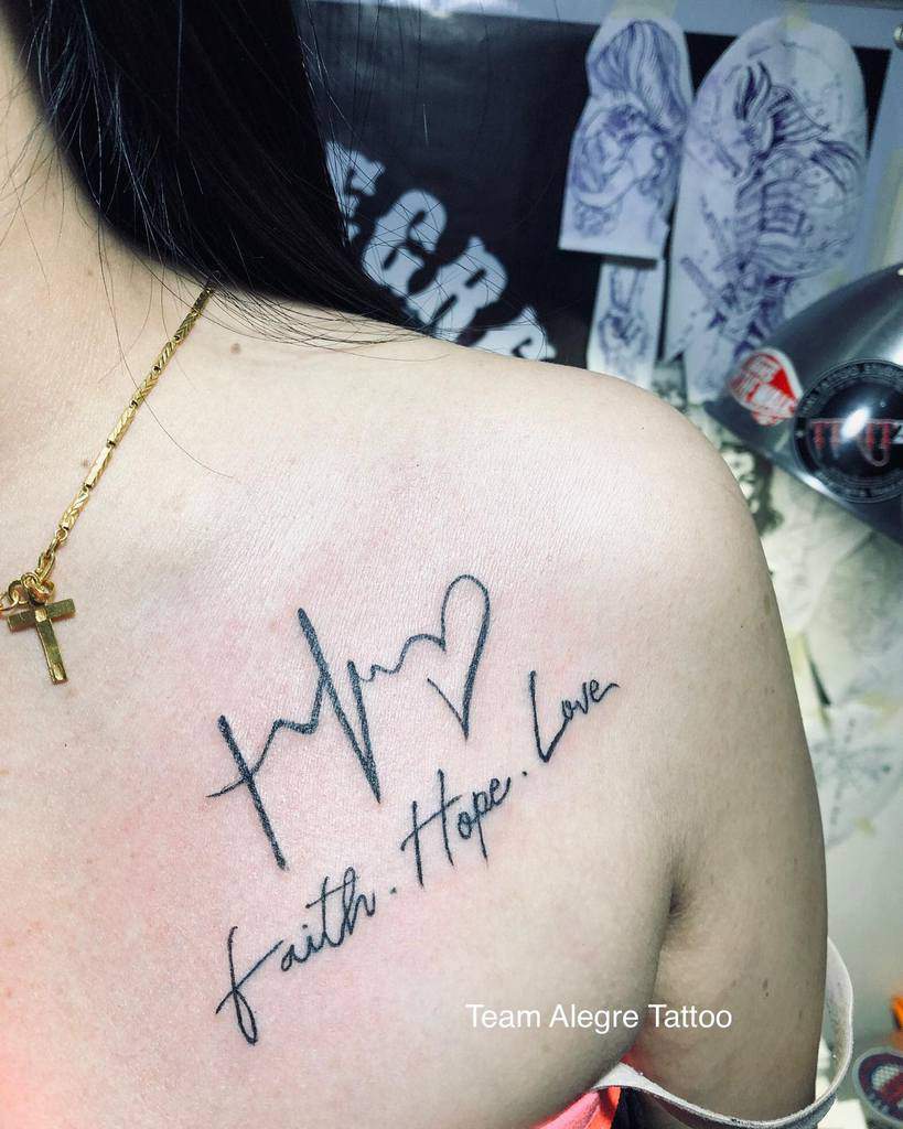 Shoulder tattoo elegantly showcasing a heartbeat line, heart symbol, and the inspiring words "faith, hope, love" in graceful script
