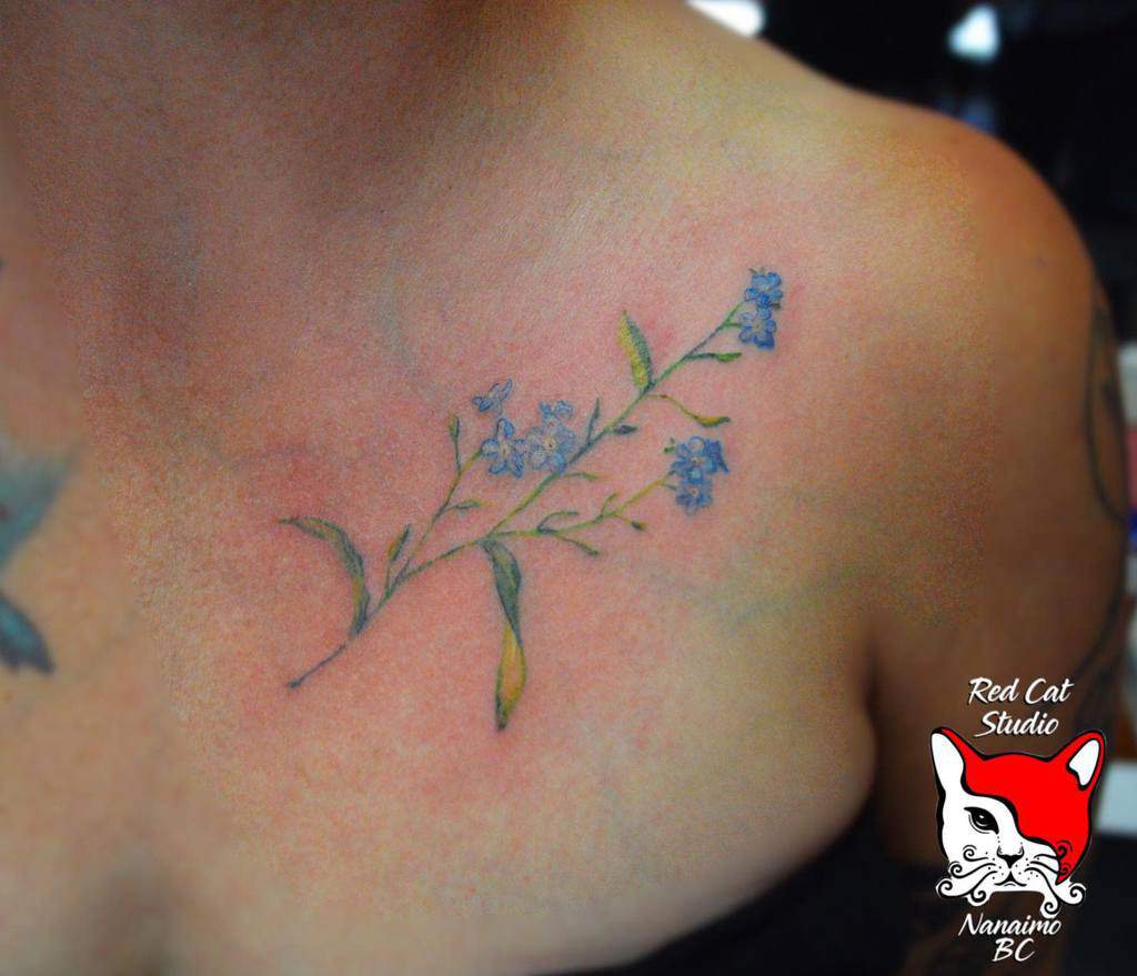 A tattoo of delicate blue forget-me-nots on a woman's shoulder