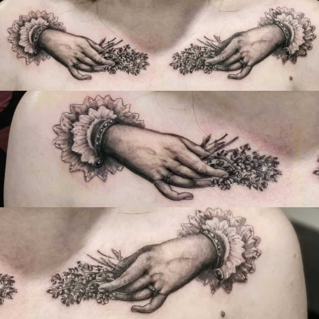 A detailed black and white tattoo of a hand holding a bundle of lavender, with intricate shading and a ruffled sleeve, placed across the chest and collarbone.