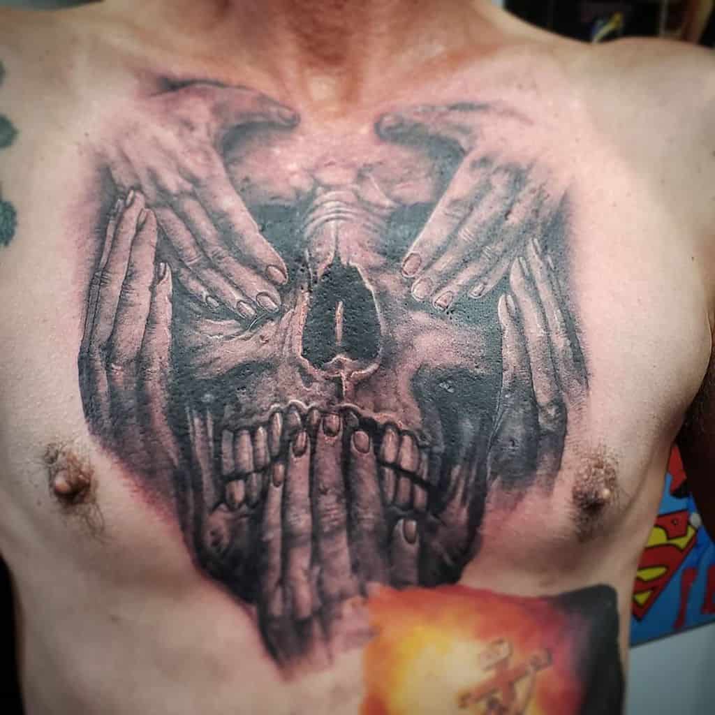 Chest tattoo of a skull formed by hands covering eyes, ears, and mouth