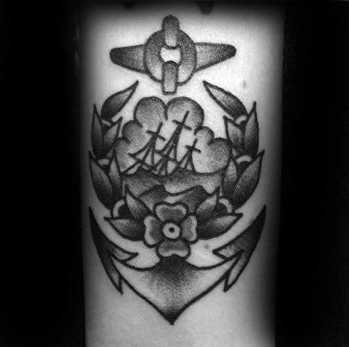 Black and grey shipwreck tattoo with a sinking ship, laurel wreath, anchor, and flower, done in bold traditional shading style.