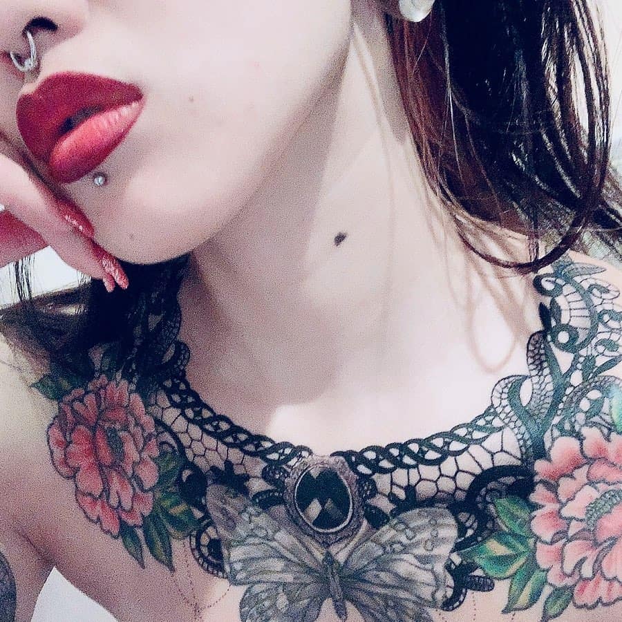 Intricate lace-style chest tattoo featuring a butterfly, roses, ornamental filigree, and a gothic pendant centerpiece.