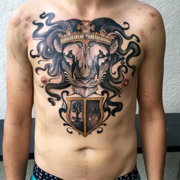 Large chest tattoo of a crowned lion's head with flowing mane, featuring a detailed crest below with symbolic designs in each shield quadrant.