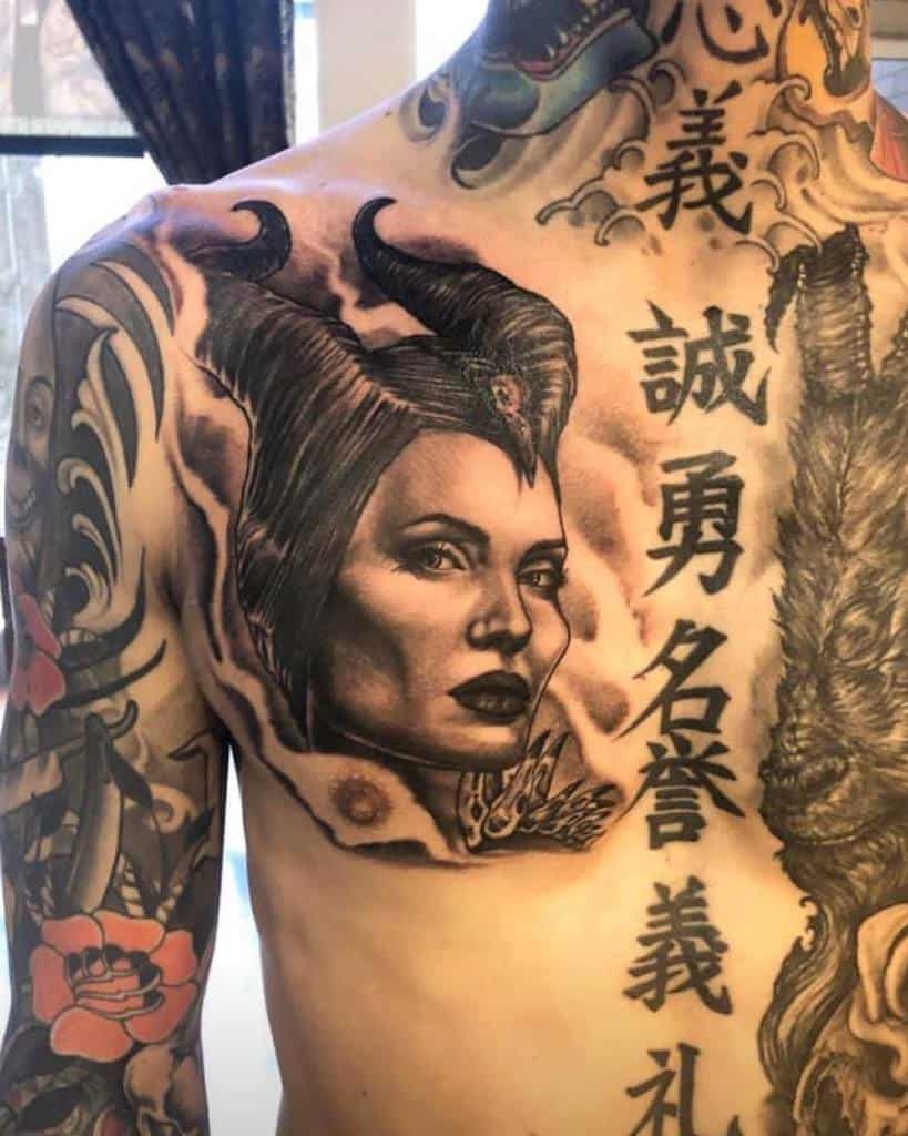 Impressive chest tattoo of Maleficent with intricate shading, framed by smoky details and surrounded by additional symbolic elements