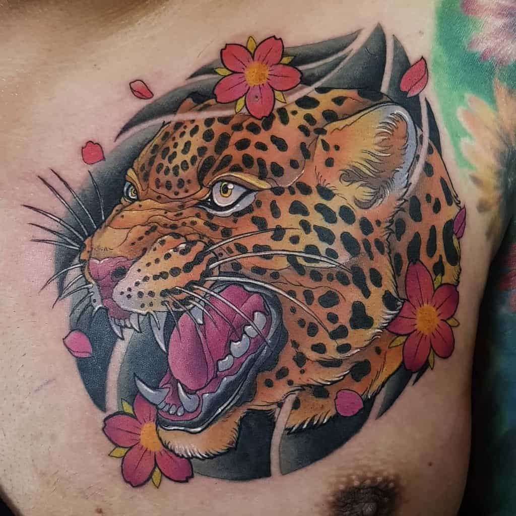 A vibrant tattoo of a roaring jaguar surrounded by colorful flowers, with petals scattered around, placed on the chest for a bold and dynamic design.
