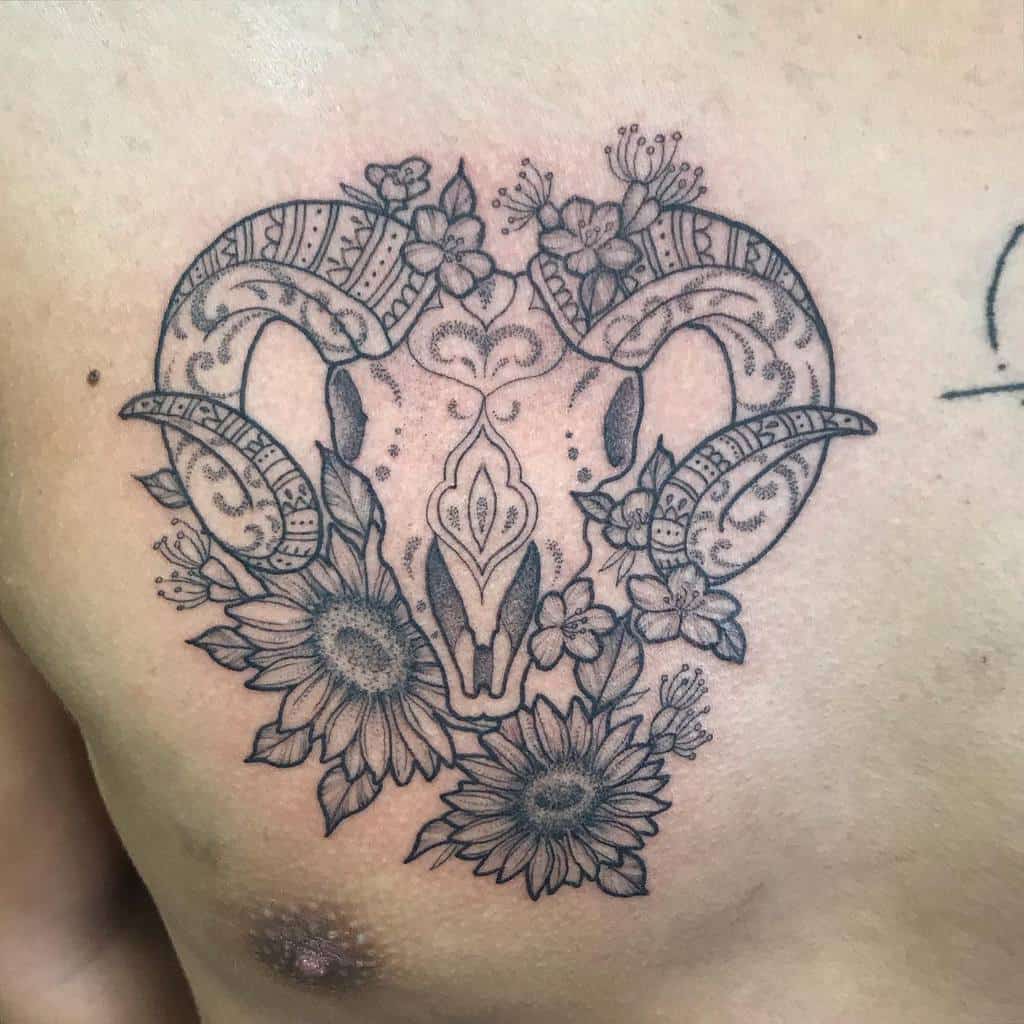 Black ink tattoo of a ram skull adorned with intricate floral patterns and detailed sunflowers on the chest