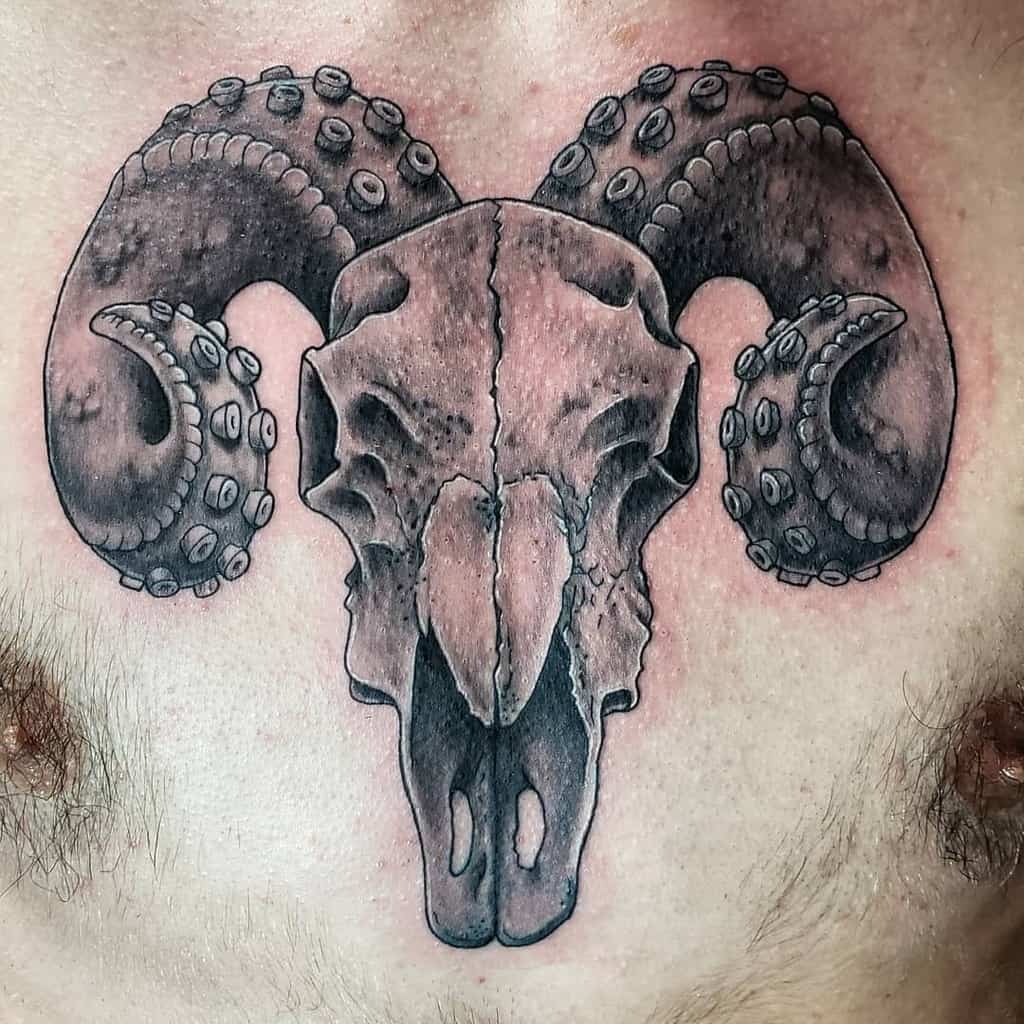 A tattoo of a stylized ram skull with tentacle-like horns adorns the person's chest