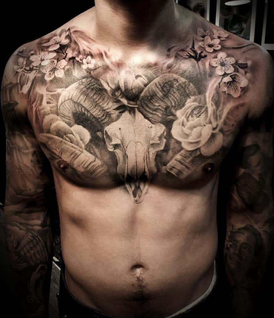 Tattooed man's chest boasting a striking ram skull, surrounded by flowers and intricate designs on a muscular torso