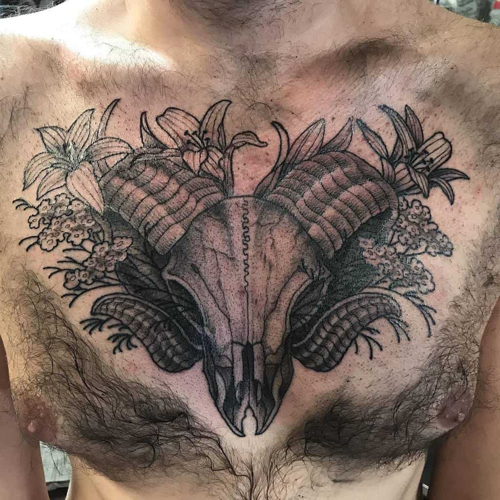 Chest tattoo of a ram skull with curved horns, intricately surrounded by an array of flowers and delicate foliage