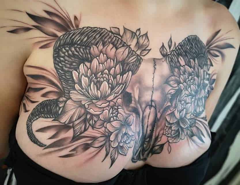 A chest tattoo featuring an intricate ram skull elegantly surrounded by ornate flowers and foliage