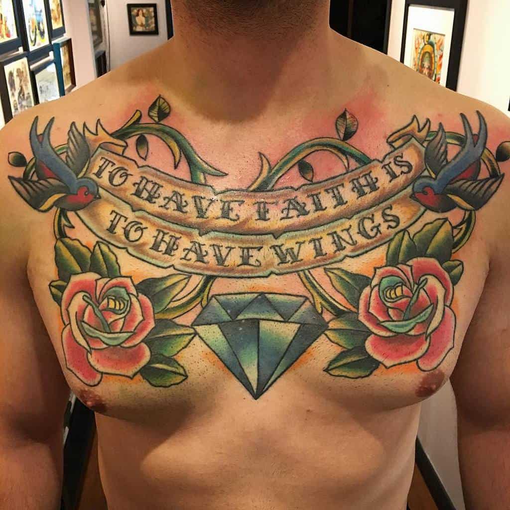 Vibrant chest tattoo featuring roses, swallows, a diamond, and the quote 'To Have Faith Is To Have Wings,' blending tradition and bold color