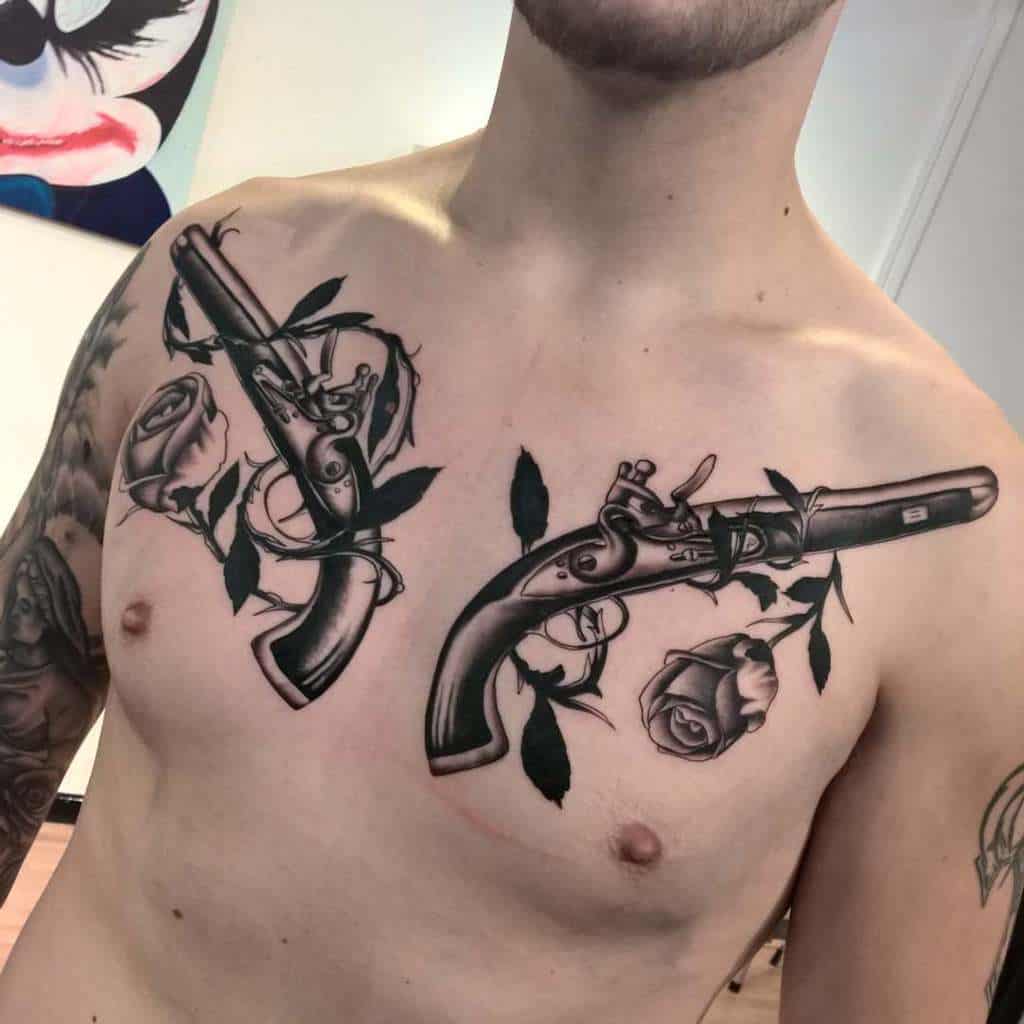 Chest tattoo featuring two detailed pistols intertwined with rose vines, showcasing bold shading and intricate floral accents