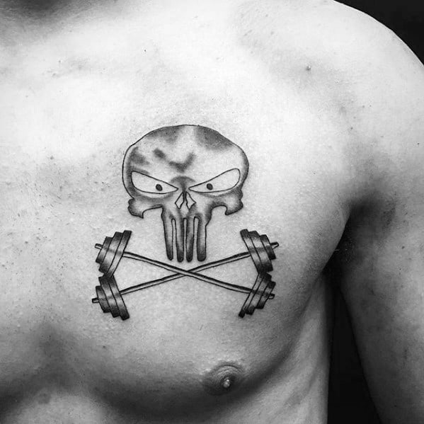 Skull tattoo with intense eyes above two crossed barbells on chest, symbolizing power, grit, and a warrior’s mindset in training.