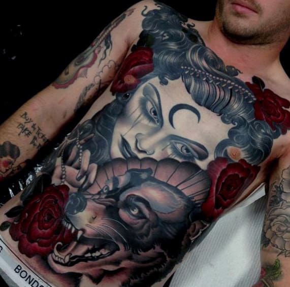 Man with intricate chest and arm tattoos featuring a woman's face, roses, and a wolf
