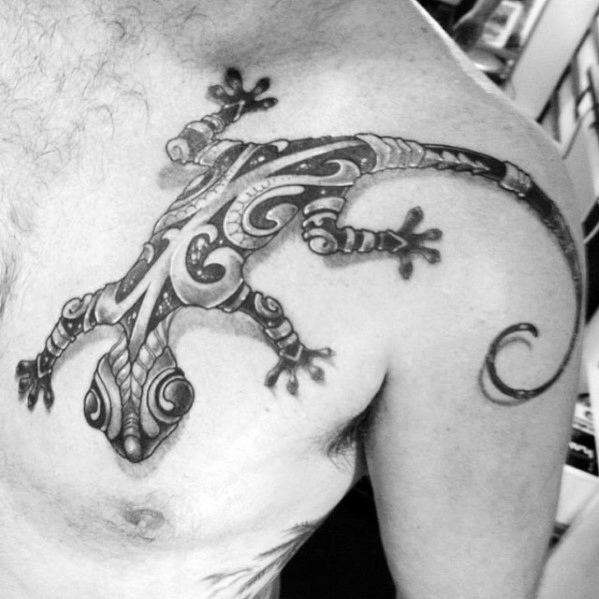 Detailed gecko tattoo on chest with tribal-inspired swirls, bold shading, and a curled tail stretching toward the shoulder.
