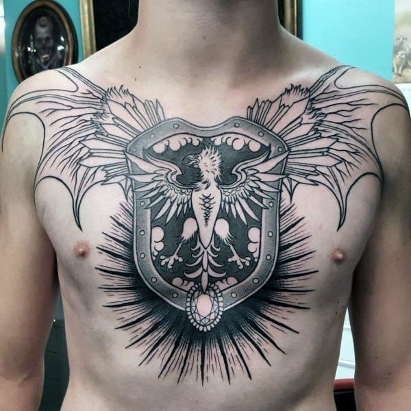 Striking chest tattoo of a stylized shield with a phoenix-like bird, extended wings, and bold black rays radiating from the center.
