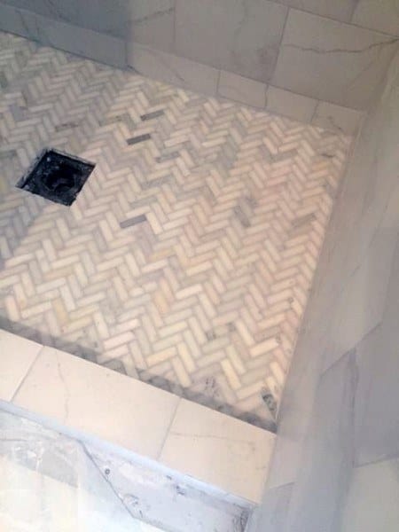 Herringbone marble tiles on a shower floor with white marble walls.