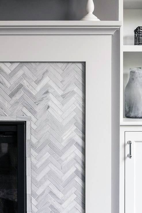 White fireplace with a herringbone tile surround and built-in shelving nearby.