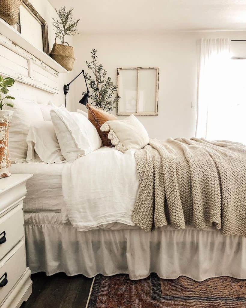 Cozy bedroom with neutral tones, layered bedding, plants, and a rustic headboard in a bright, airy space