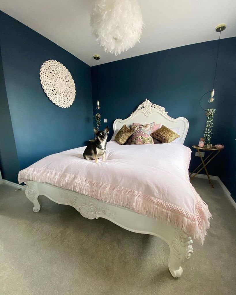 Ornate bedroom with dark blue walls, white bed, pink bedding, and a small dog sitting on the bed