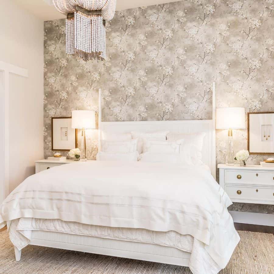Elegant bedroom with floral wallpaper, white bed, two lamps on nightstands, and a chandelier above