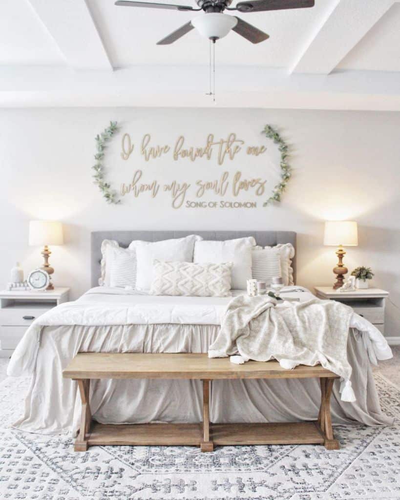 Cozy bedroom with a bed, wooden bench, lamps, and wall art quoting Song of Solomon; neutral tones and soft décor