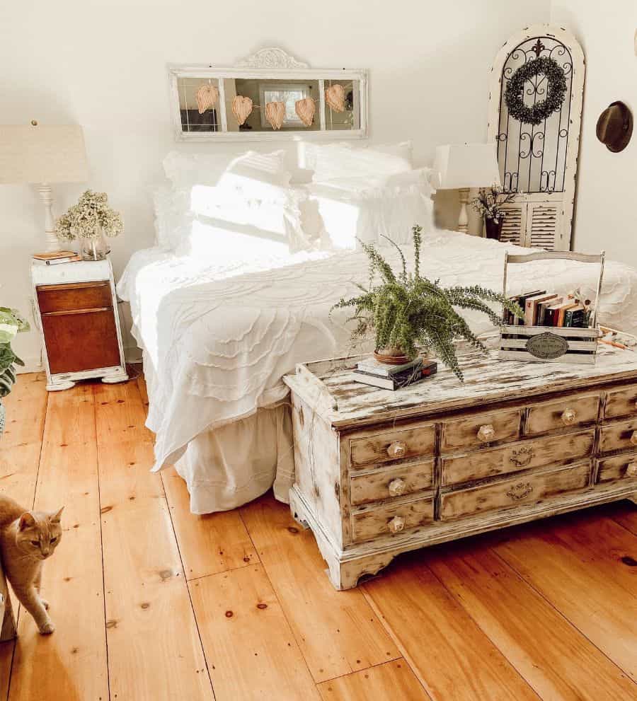 Cozy farmhouse bedroom with a rustic wooden bed, a fern on a chest, and a cat on the wooden floor