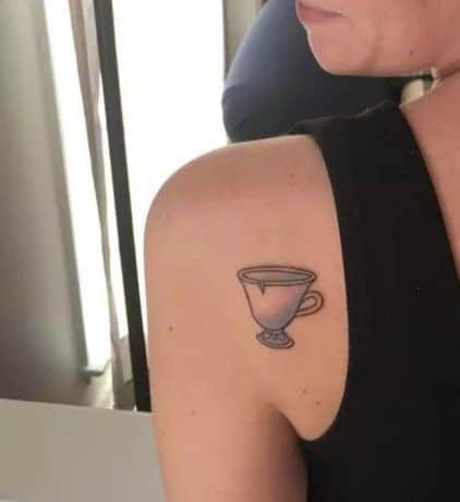 Minimalist tattoo of Chip, the enchanted teacup from Beauty and the Beast, placed on the upper shoulder with simple linework.