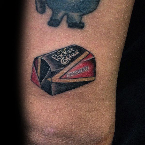 Realistic tattoo of a Pocket Coffee chocolate piece on the arm, featuring detailed shading and highlights for a three-dimensional effect.