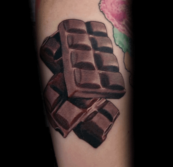 Realistic tattoo of stacked chocolate pieces with detailed shading and highlights, creating a 3D effect on the skin.