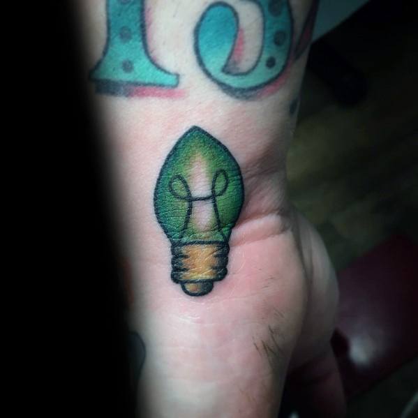 Minimalist Christmas tattoo of a green holiday light bulb on the wrist, featuring simple shading and bold outlines for a subtle festive touch.