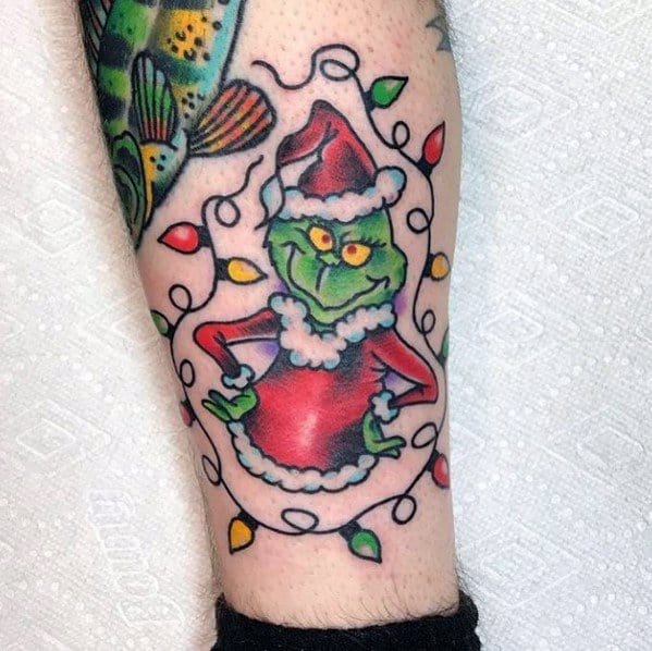 Christmas tattoo of the Grinch in a Santa outfit, smirking mischievously, surrounded by colorful holiday lights for a playful and festive holiday design.