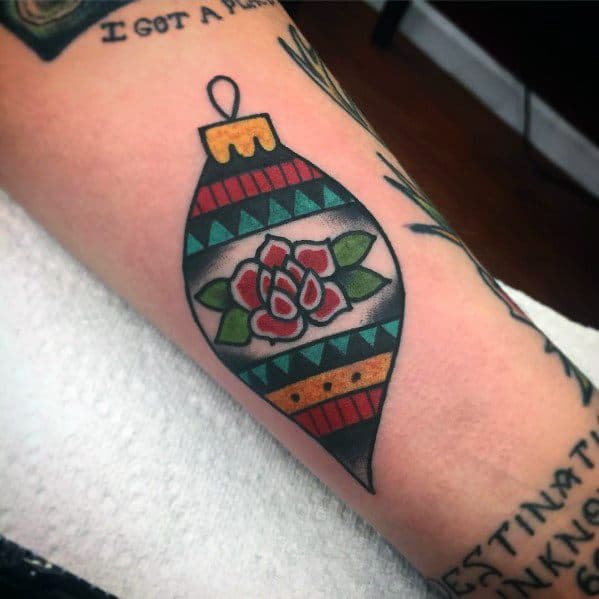 Traditional-style Christmas tattoo of a vintage ornament with a floral design and geometric patterns, featuring bold lines and festive colors.