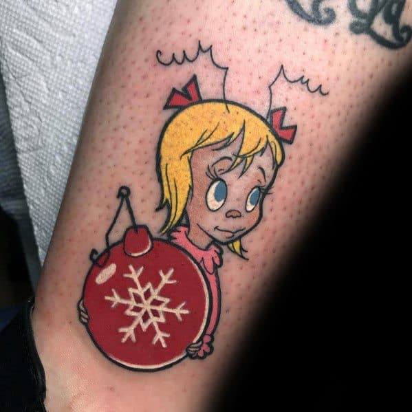 Christmas tattoo of Cindy Lou Who from *How the Grinch Stole Christmas*, holding a red ornament with a snowflake design, featuring a classic cartoon style.