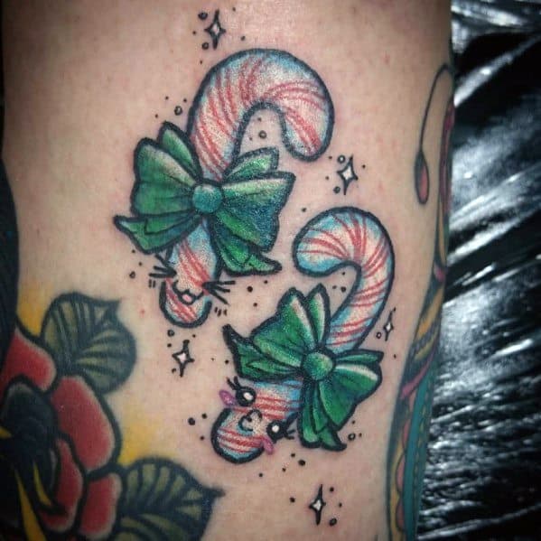 Playful Christmas tattoo of two candy canes with cat-like faces, adorned with green bows and sparkles, blending holiday charm with a whimsical touch.