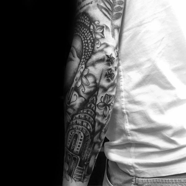 Chrysler Building sleeve tattoo combined with floral patterns and a serene Buddha portrait in black-and-grey for a tranquil aesthetic.