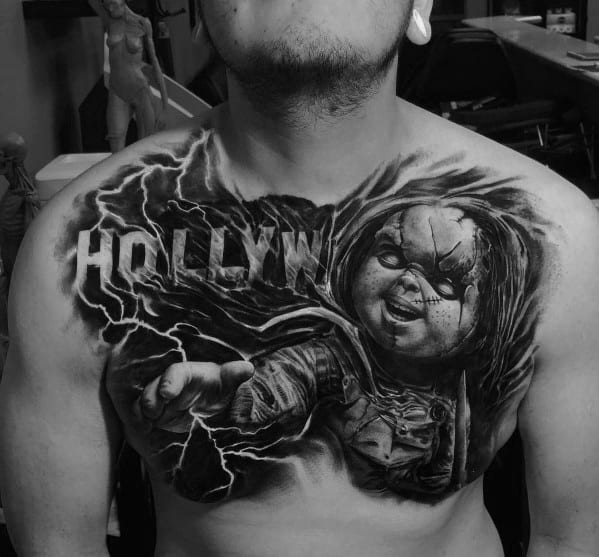 Black and grey Chucky chest tattoo with dramatic lightning, eerie shading, and the word "HOLLYW" for a bold and haunting horror design.