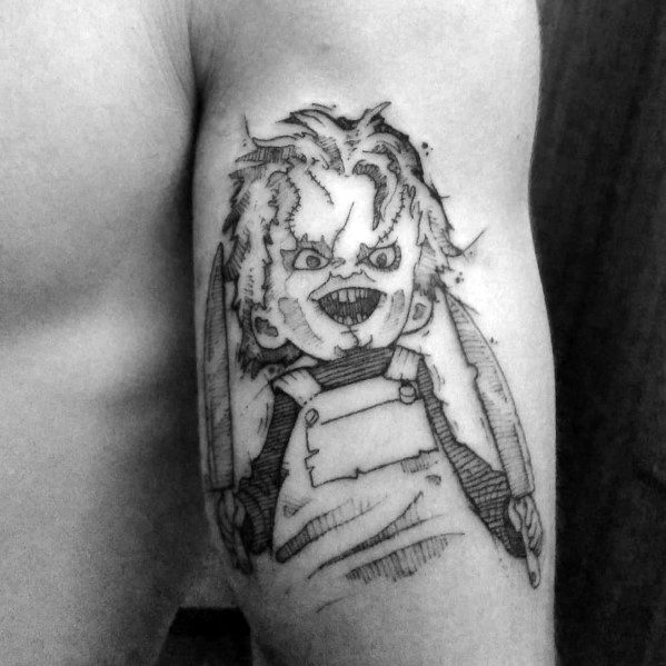 Black and grey Chucky tattoo with a sketch-style design, featuring his menacing grin, stitched face, and two knives for a bold horror look.