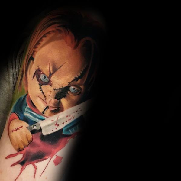 Realistic Chucky tattoo with intense blue eyes, stitched face, and a bloodied knife, creating a striking and terrifying horror design.