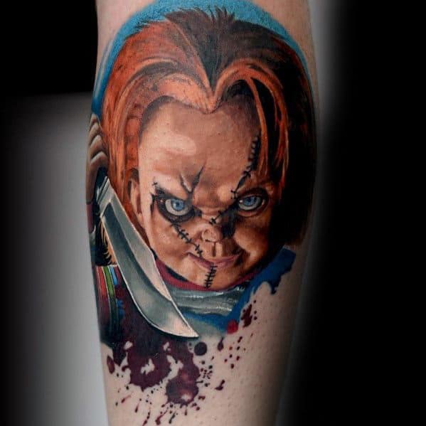 Realistic Chucky tattoo with piercing blue eyes, stitched face, and a bloodied knife, set against a bold blue background for a dramatic effect.
