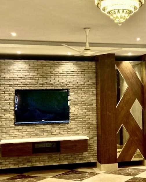 Cinder block wall with mounted TV, wooden accents, and chandelier in a modern living room.