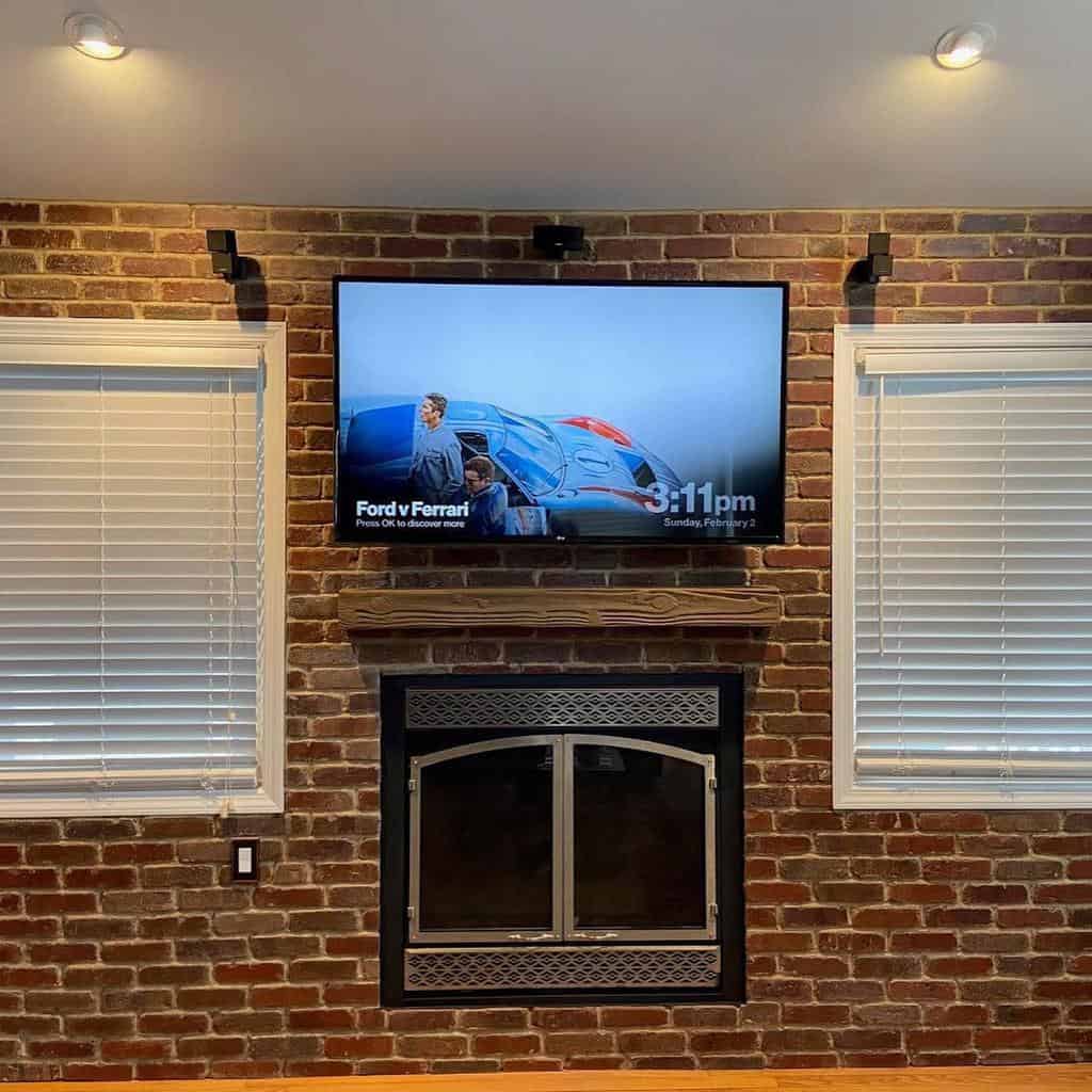 Exposed brick living room wall with mounted TV and fireplace underneath.
