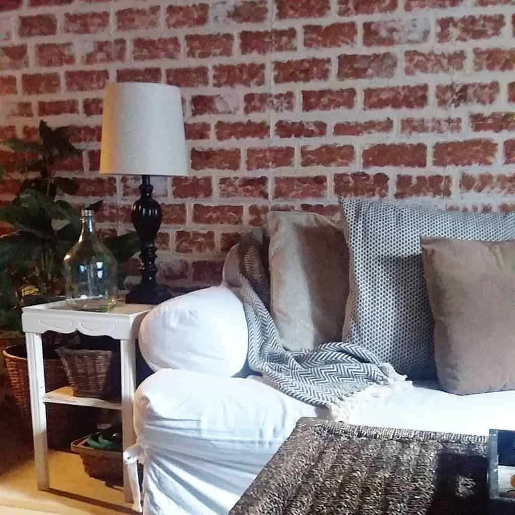 Cozy living room with exposed brick wall, white couch, side table, and decorative lamp.