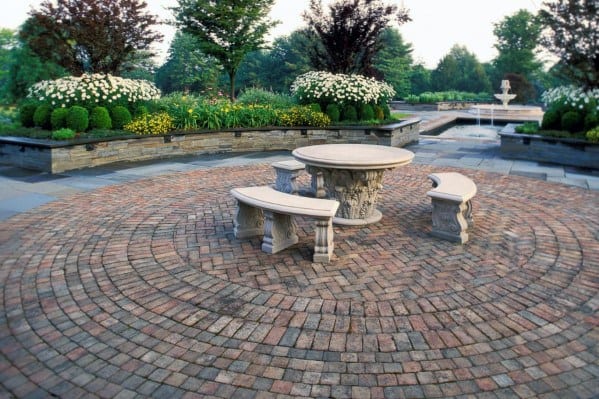 Circular brick patio with stone table, brick benches, and lush garden background