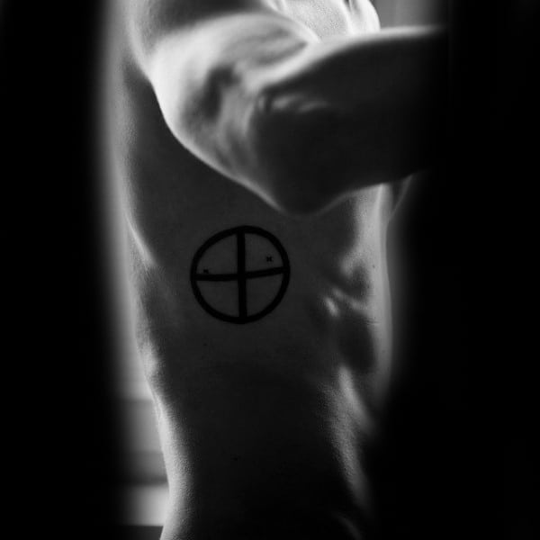 Close-up of a person's side with a circular tattoo featuring cross lines